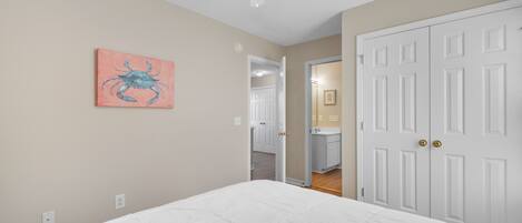 A bedroom with a bed, a ceiling fan, a door, and a hallway leading to a bathroom.