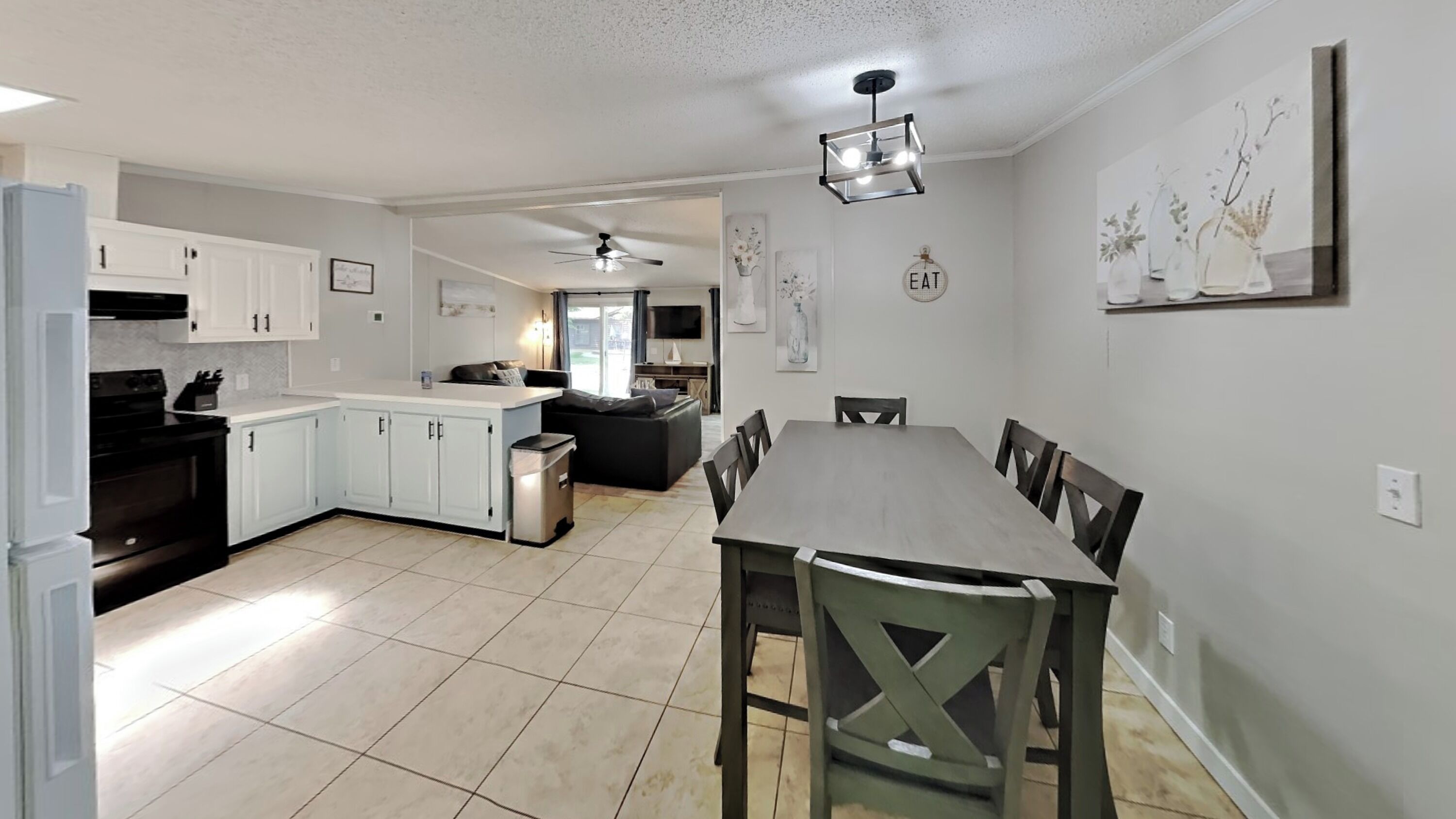 A modern kitchen with white cabinets, a dining table with chairs, and a ceiling fan.
