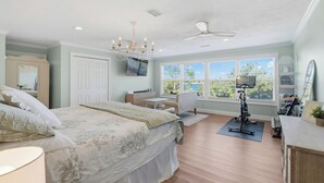 Ein Schlafzimmer mit einem großen Bett, einem Schreibtisch, einem Stuhl, einem Deckenventilator und einem Fenster mit Blick auf Bäume.