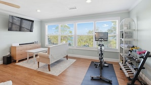 Ein Heim-Fitnessraum mit Trainingsgeräten, einer Couch und einem großen Fenster mit Aussicht.
