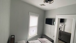 Une chambre à coucher avec un lit, une télévision, un ventilateur de plafond et une fenêtre.