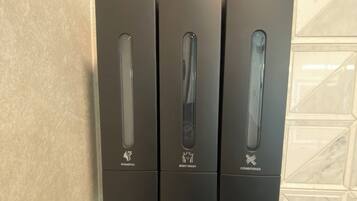 A wall-mounted dispenser with three compartments labeled for shampoo, body wash, and conditioner.