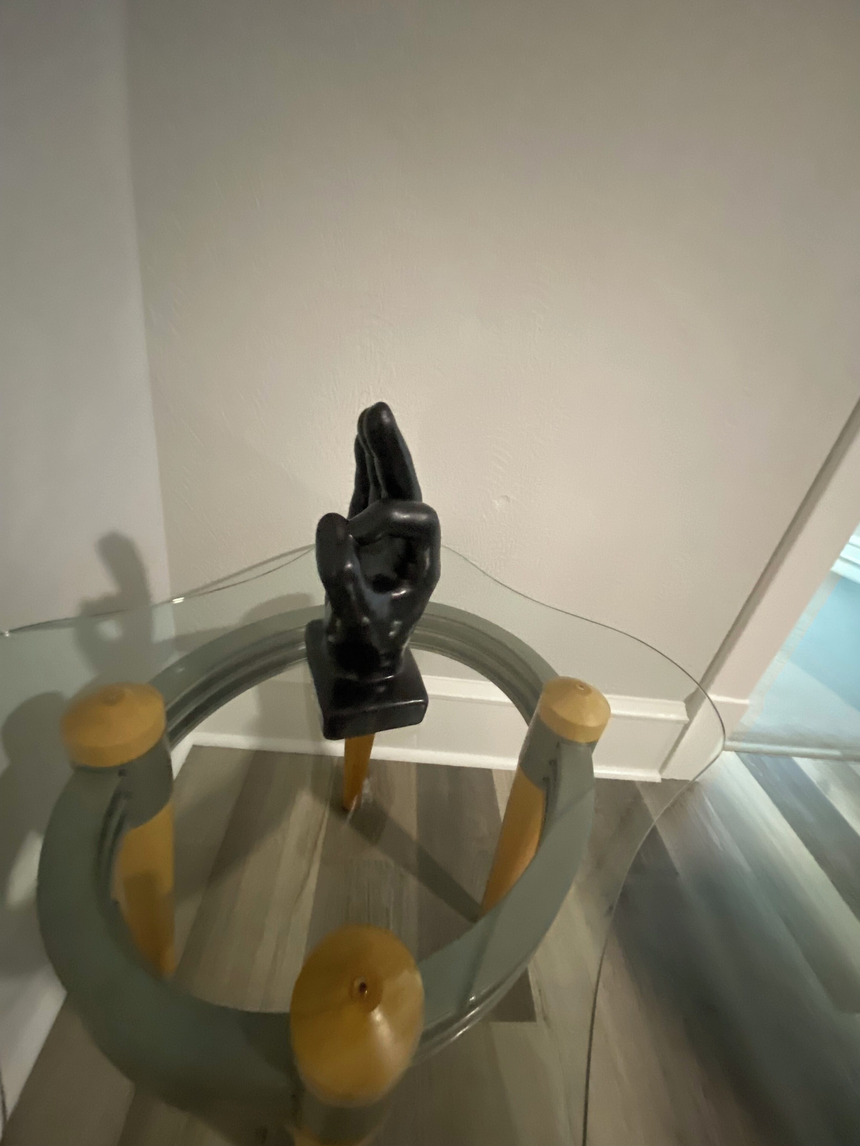 A glass table with a black sculpture in the center and wooden legs.