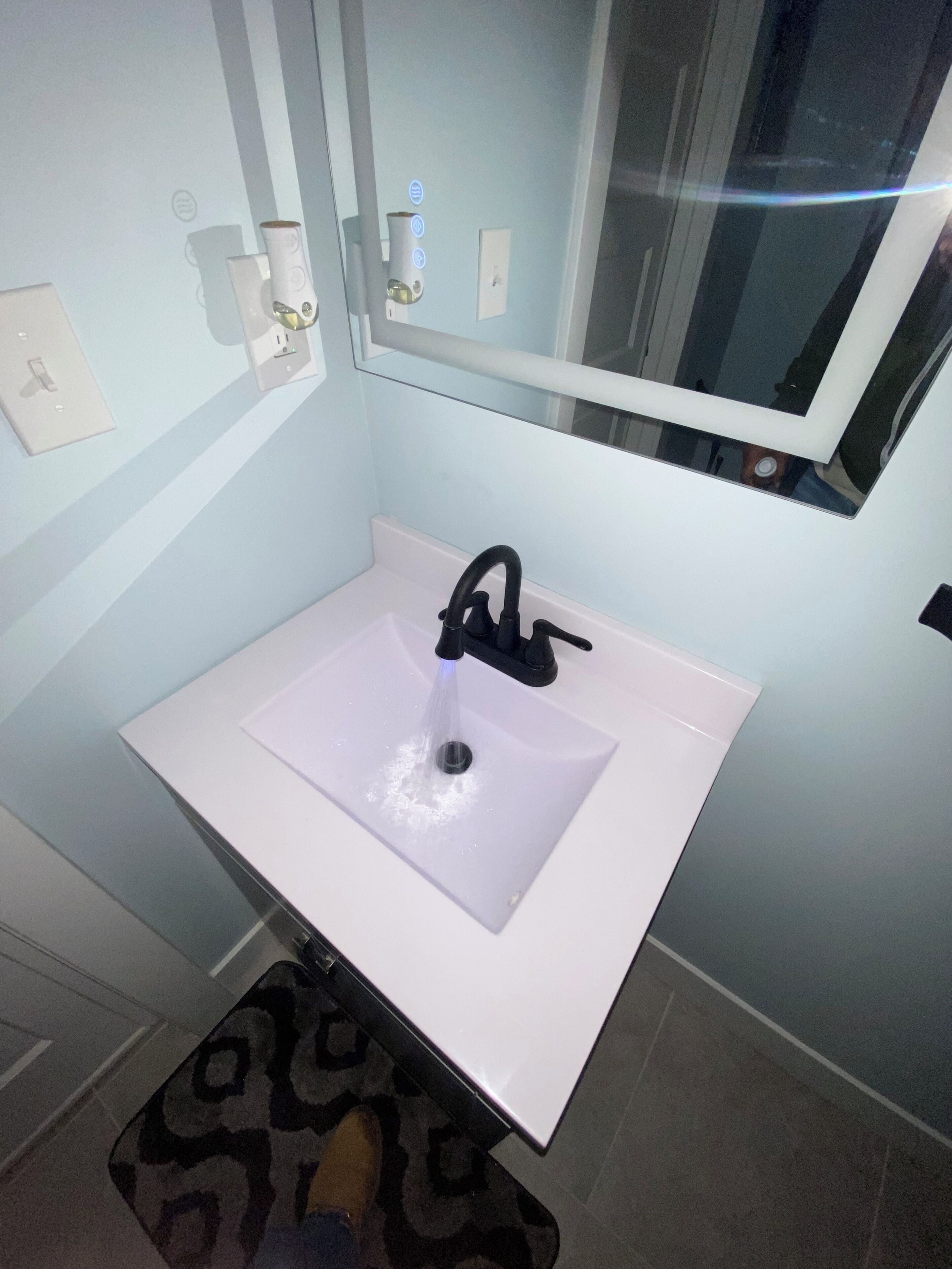 A bathroom with a white sink, a mirror above it, and a toilet visible in the background.