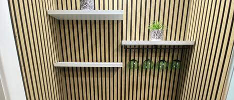 Une cuisine compacte avec un plan de travail noir, des placards blancs et un four encastré. On y trouve deux étagères blanches ornées d’objets décoratifs et une plante en pot.