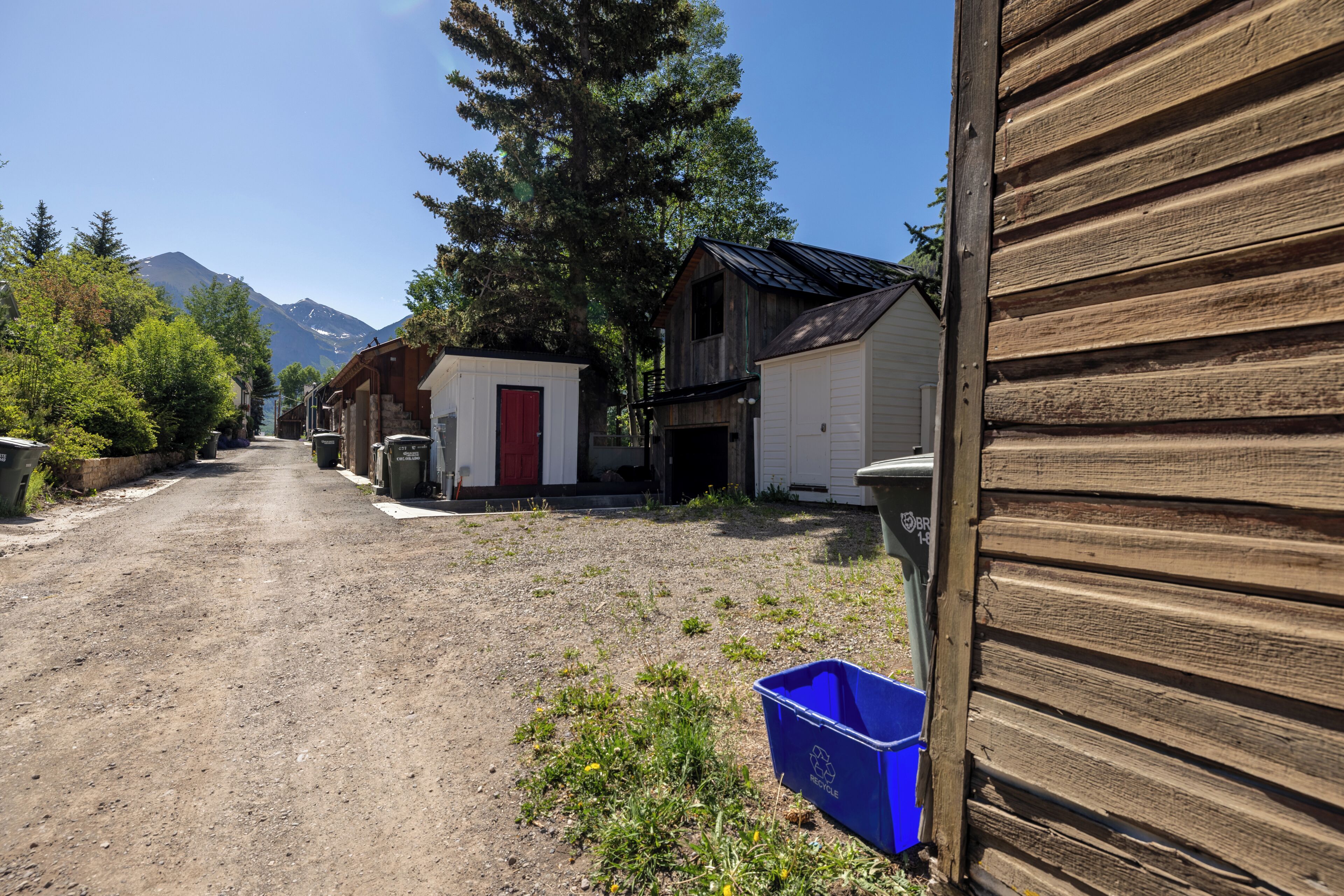 A rural street with wooden buildings, a dirt road, and a mountain in the background.