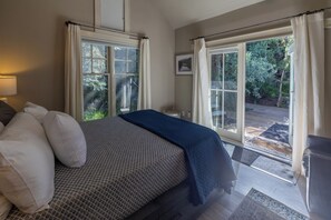 A bedroom with a bed, a nightstand, a lamp, and a view of a garden through large windows. - Your Luxury Private Telluride Getaway – Steps from Main Street & the Gondola (Telluride)