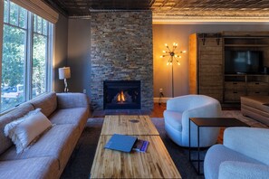 A living room with a stone fireplace, a sofa, a round chair, a coffee table, and a TV stand. - Your Luxury Private Telluride Getaway – Steps from Main Street & the Gondola (Telluride)