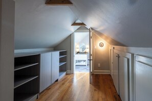 Ein schmaler Flur mit Holzdielen, weißen Wänden und einer schrägen Decke.