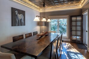 Un'area pranzo moderna con un tavolo lungo, lampade a sospensione e un dipinto a cavallo sulla parete.