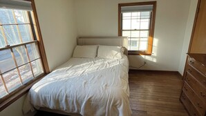 Una camera da letto con un letto, pavimento in legno, una cassettiera e una lampada a soffitto.
