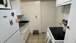 Een kleine keuken met witte kasten, een koelkast, een fornuis en een spoelbak.