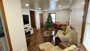 Un ampio soggiorno con pavimento in legno, un grande albero di Natale e un'accogliente area salotto con mobili in vimini.
