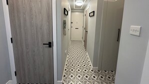 Un couloir avec un sol à motifs, une porte en bois et un interrupteur sur le mur.
