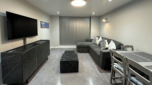 Un salon moderne doté d’un téléviseur à écran plat, d’un canapé d’angle, d’une table basse en marbre et d’un coin repas avec un banc.