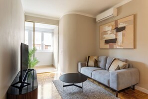 A modern living room with a grey sofa, a black coffee table, and a large abstract painting on the wall. - Descubre tu nuevo hogar en pleno corazón de Madrid, en la vibrante calle Orense. Este elegante apartamento de 50 m² ha sido diseñado para ofrecer confort, estilo y funcionalidad en cada rincón. (MADRID)