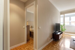 A modern living room with a flat-screen TV, a wooden floor, and a large window. - Descubre tu nuevo hogar en pleno corazón de Madrid, en la vibrante calle Orense. Este elegante apartamento de 50 m² ha sido diseñado para ofrecer confort, estilo y funcionalidad en cada rincón. (MADRID)