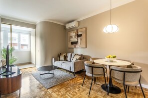 A modern living room with a sofa, a round dining table with chairs, a coffee table, a TV stand, and a hanging light fixture. - Descubre tu nuevo hogar en pleno corazón de Madrid, en la vibrante calle Orense. Este elegante apartamento de 50 m² ha sido diseñado para ofrecer confort, estilo y funcionalidad en cada rincón. (MADRID)