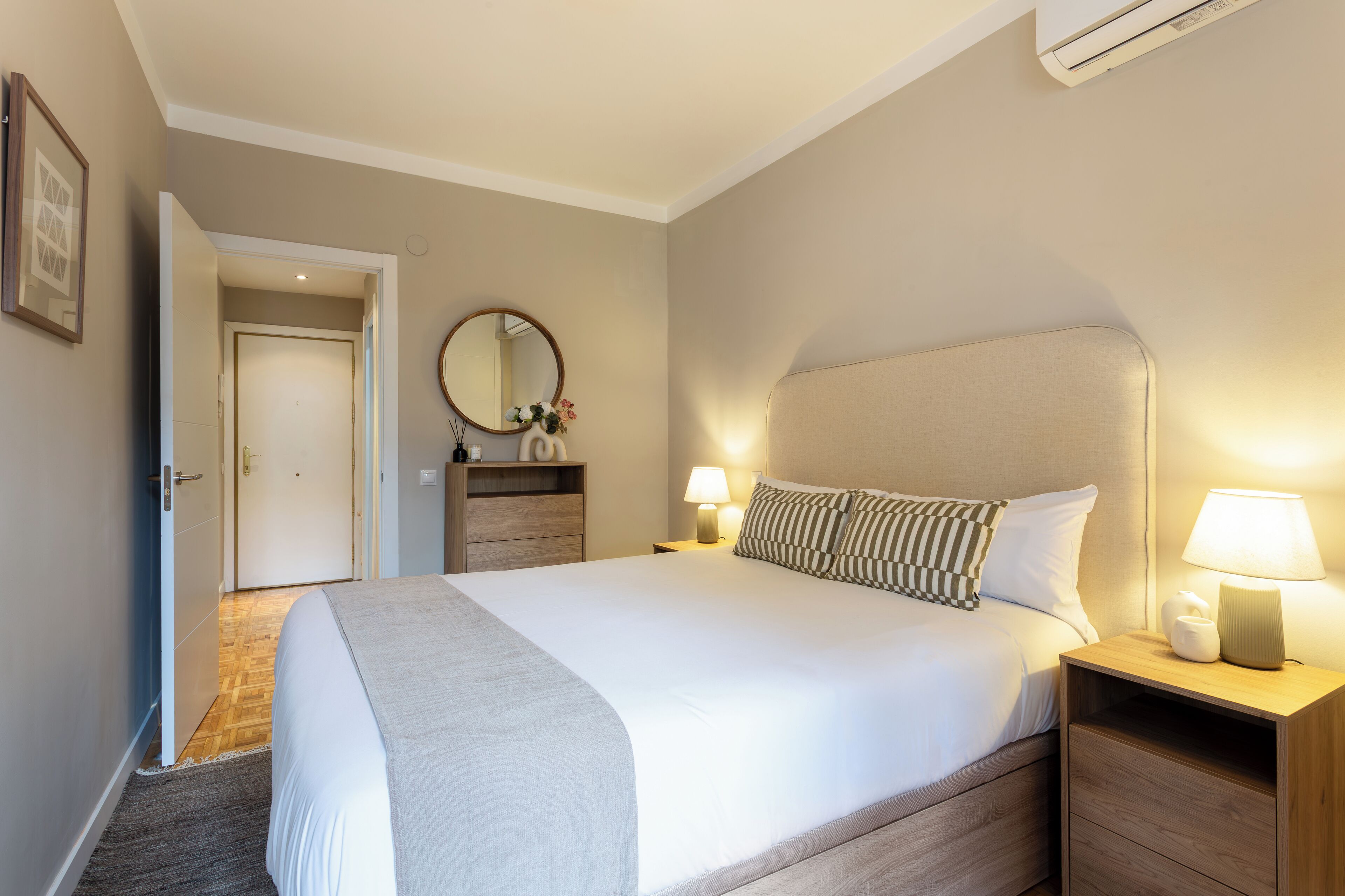 Une chambre à coucher bien rangée, avec un grand lit, des tables de chevet avec des lampes, un miroir et une porte donnant sur une autre pièce.