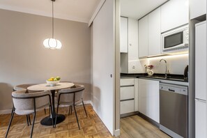 A compact kitchen with a microwave, dishwasher, and a dining area with a round table and chairs. - Descubre tu nuevo hogar en pleno corazón de Madrid, en la vibrante calle Orense. Este elegante apartamento de 50 m² ha sido diseñado para ofrecer confort, estilo y funcionalidad en cada rincón. (MADRID)