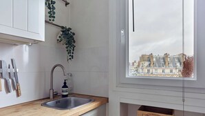 Cozinha com bancada de madeira, pia de aço inoxidável e janela com vista para edifícios.