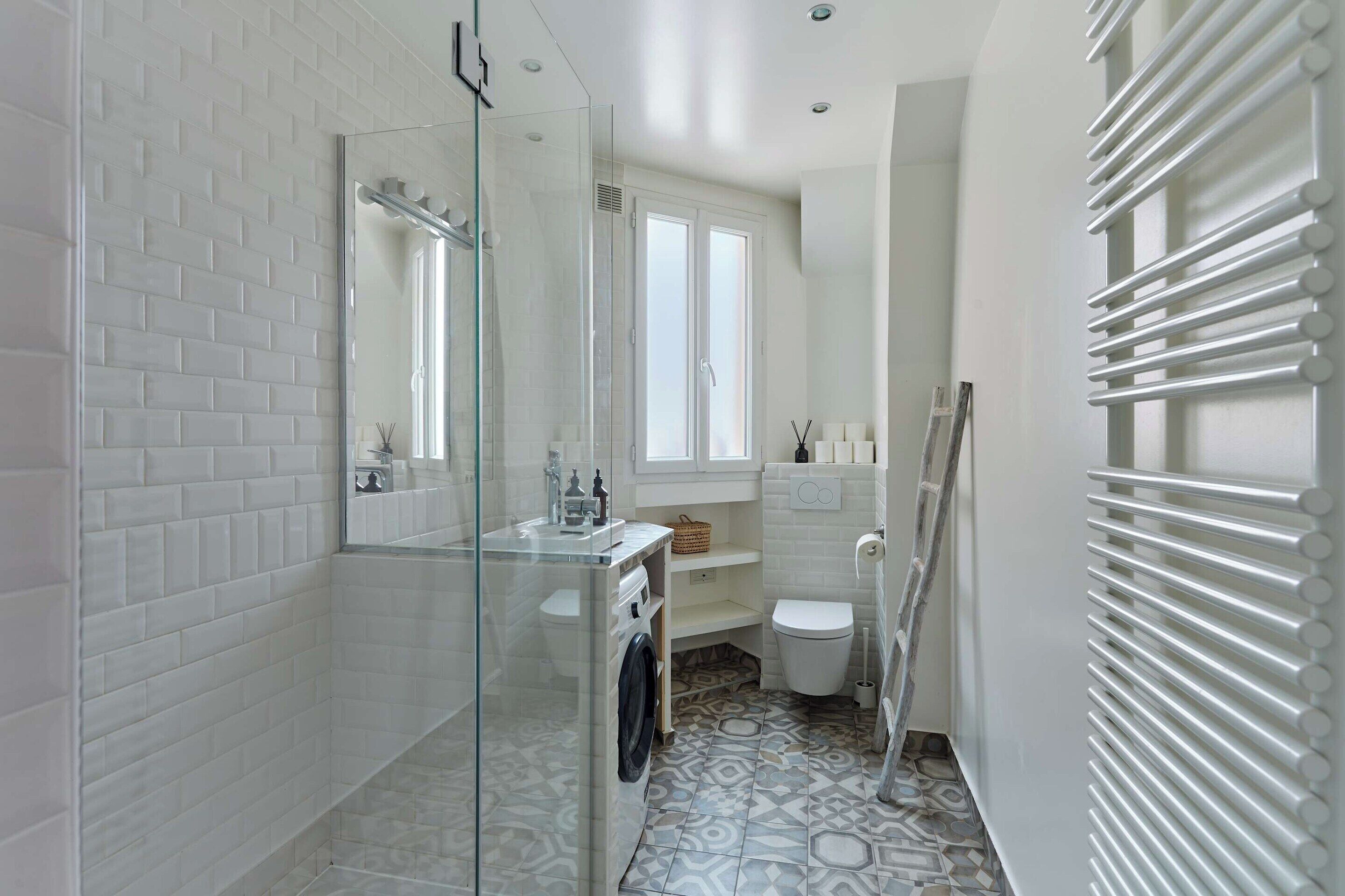 A modern bathroom with a glass shower enclosure, a built-in washing machine, a toilet, and a radiator.