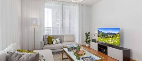 A modern living room with a sofa, coffee table, and a TV displaying a scenic landscape.