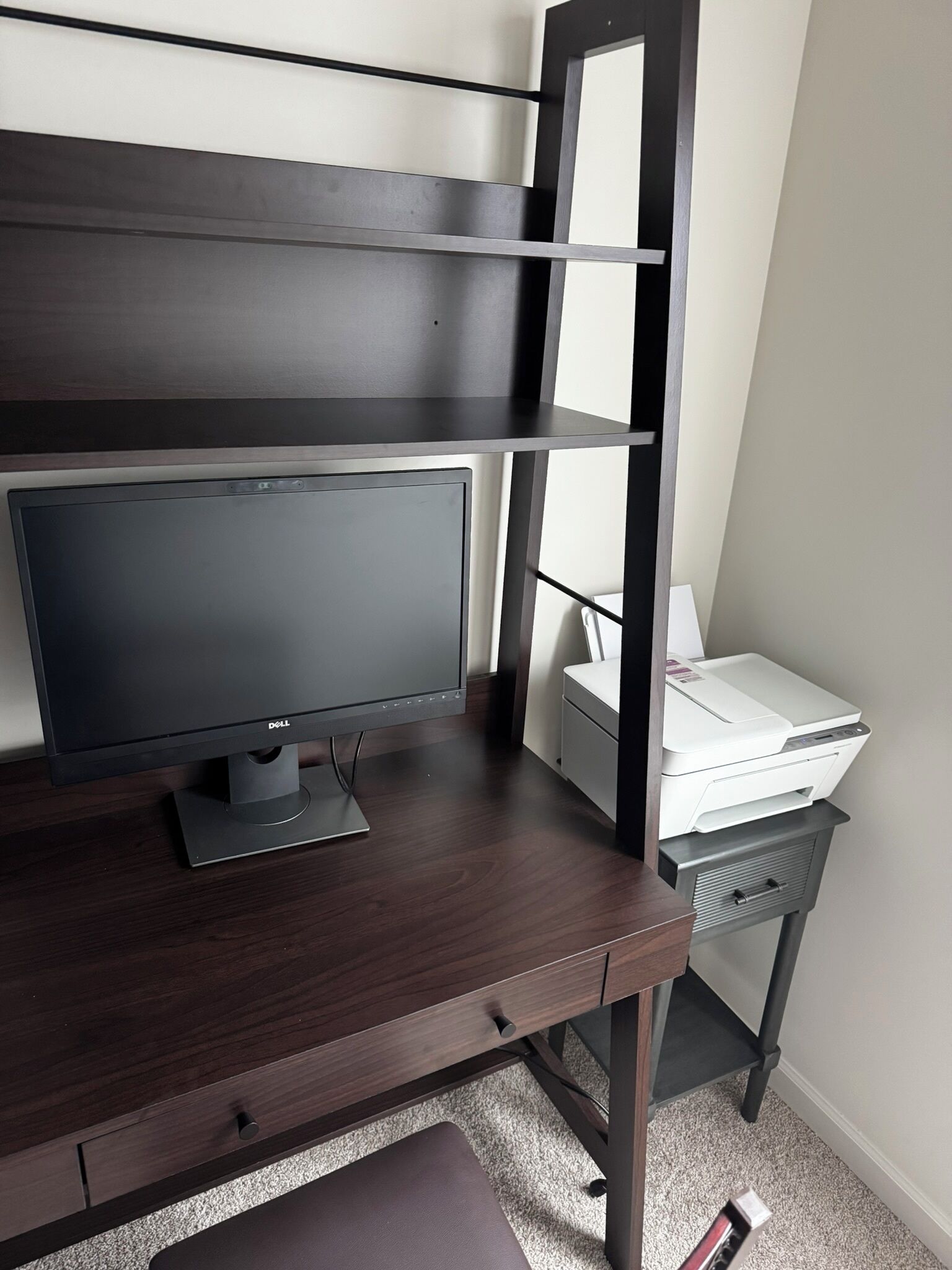 Un escriptori de fusta fosca amb un monitor de pantalla plana, una impressora i una petita estanteria.