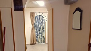 A hallway with a tiled floor, a door on the left, a blue basket on the right, and a mirror on the wall. - Wine Vanult Apartment Tbilisi (T'bilisi)