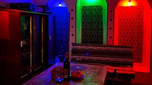 A dining area with a table, chairs, and a bench. There is a cabinet with items on top. The room has a unique lighting design with colored lights. - Wine Vanult Apartment Tbilisi (T'bilisi)