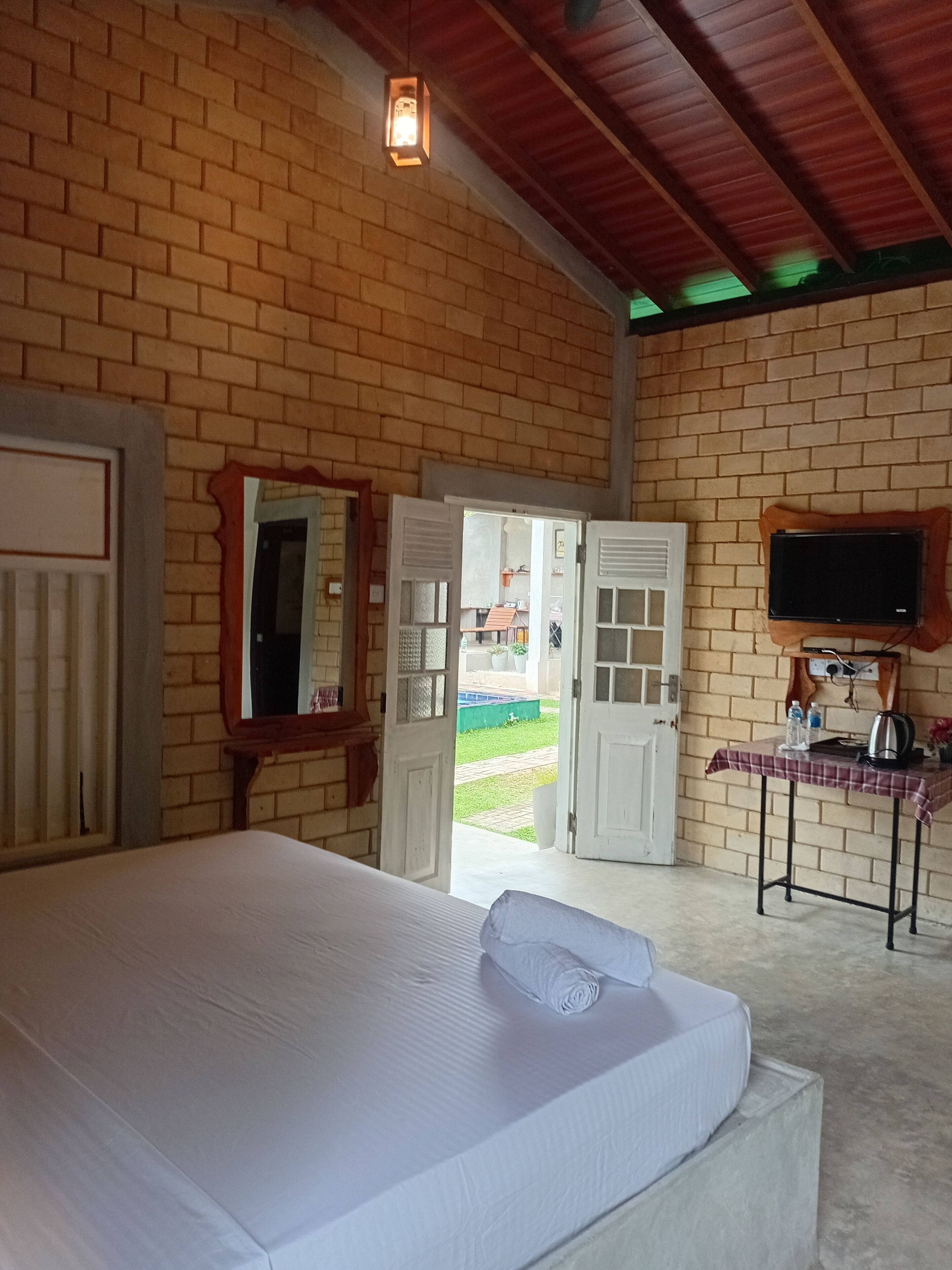 A room with a bed, a television mounted on the wall, and a table with a kettle and water bottles.
