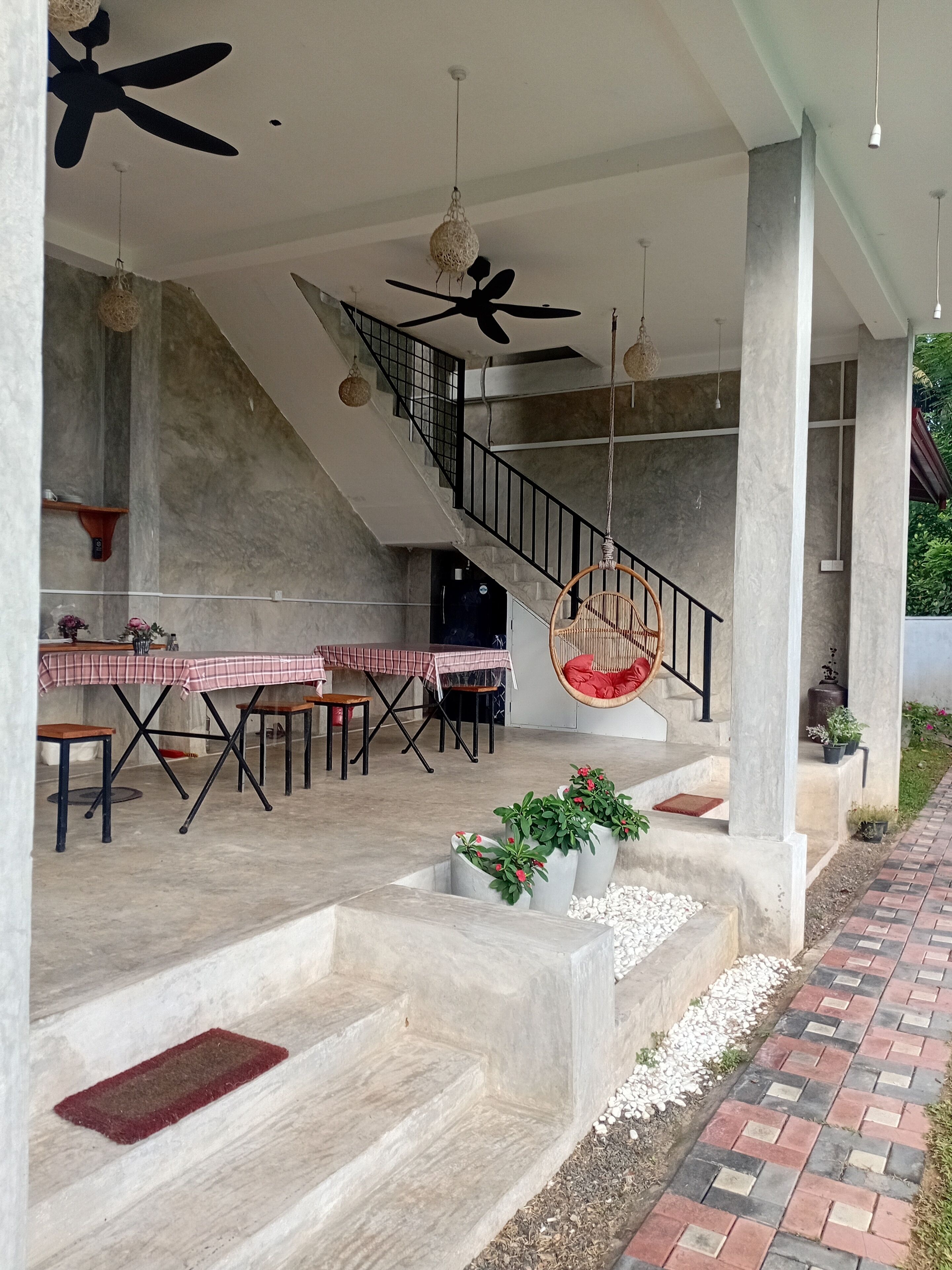 Un espace extérieur abrité comprenant une table à manger, un escalier, des fauteuils suspendus et des plantes en pot.