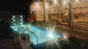 A swimming pool with a red car parked nearby, a covered outdoor seating area, and a building with a brick facade. - Light villa galle (Galle)
