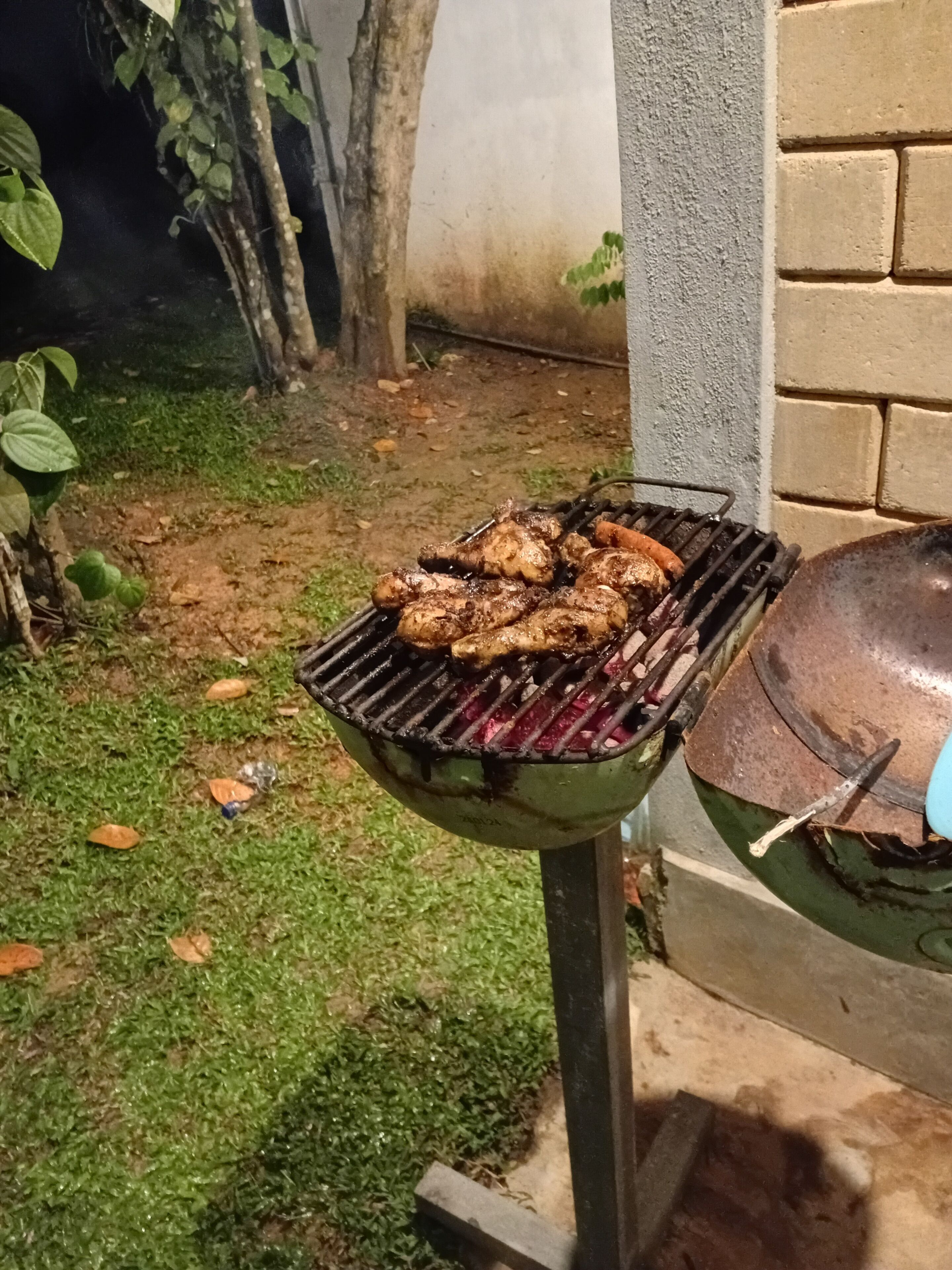 A barbecue grill with chicken and sausages being cooked outdoors.