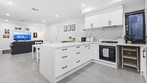 A modern kitchen with white cabinetry, a built-in oven, and a dining area with a white table and chairs. - Premium Modern Homestay-Walk to Curtin University (Saint James)