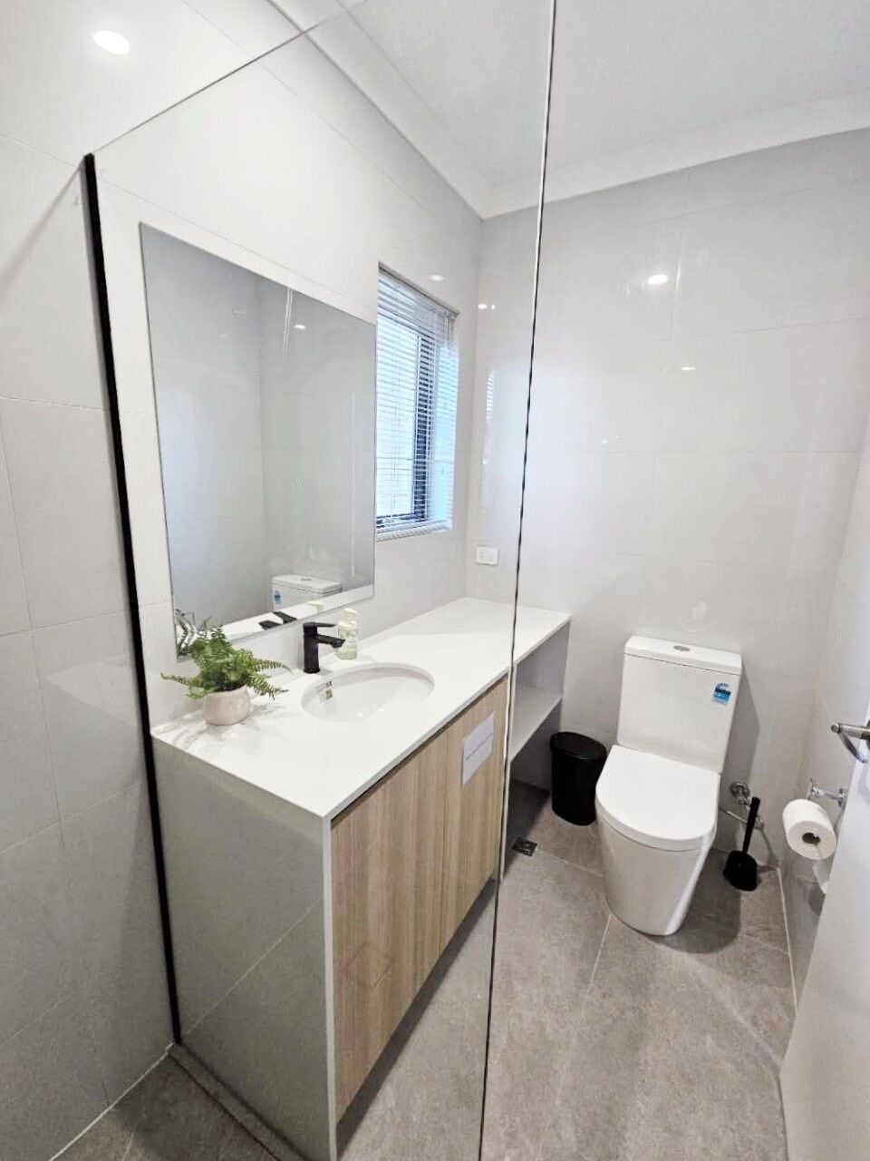 A modern bathroom with a large mirror, white sink, and toilet.