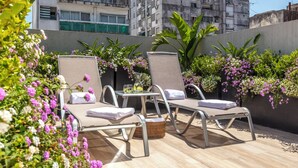 Eine Dachterrasse mit zwei Liegestühlen, einem kleinen Tisch und einem Korb.