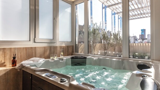 Ein modernes Badezimmer mit einer großzügigen Badewanne, einer Duschkabine aus Glas und Blick auf die Stadt durch große Fenster.