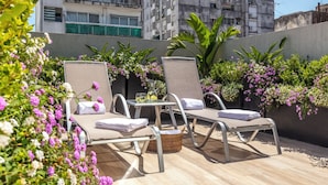 Eine Dachterrasse mit zwei Liegestühlen, einem kleinen Tisch und einem Korb.