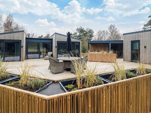 A modern outdoor patio with a wooden deck, built-in seating, and a central table. - 5 Star Holiday Home in Vaeggerlose (Vaeggerlose)