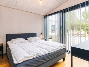 Ein Schlafzimmer mit Bett, Schreibtisch und Blick durch ein Fenster mit Lamellen.