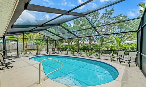 An indoor swimming pool with clear glass walls, surrounded by chairs and a covered area.
