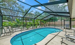 An indoor swimming pool with a glass enclosure, surrounded by chairs and plants.