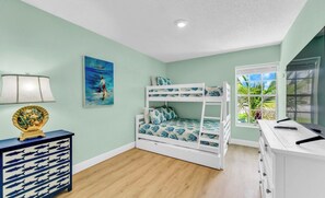 A room with a bunk bed, a desk with a lamp, a decorative shell, and a painting of a person on a beach.