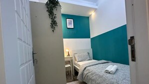 Ein kleines, ordentlich eingerichtetes Schlafzimmer mit einem Bett, einem Nachttisch mit Lampe und einem Wandbild.