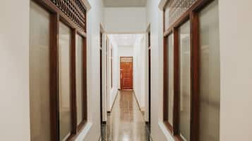 Un pasillo con una puerta de madera al final, flanqueado por paredes con molduras decorativas y un suelo de baldosas.