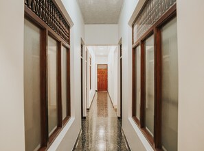 A corridor with a wooden door at the end, flanked by walls with decorative moldings and a tiled floor.