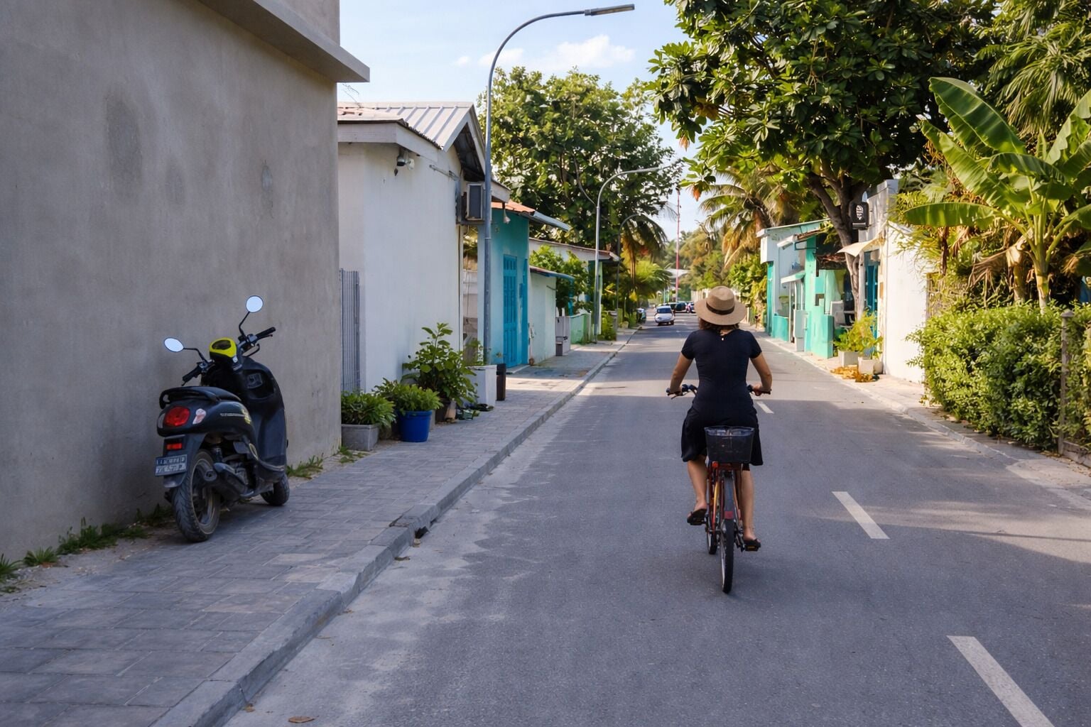 A narrow street with a person riding a bicycle, a parked scooter, and buildings with blue doors.