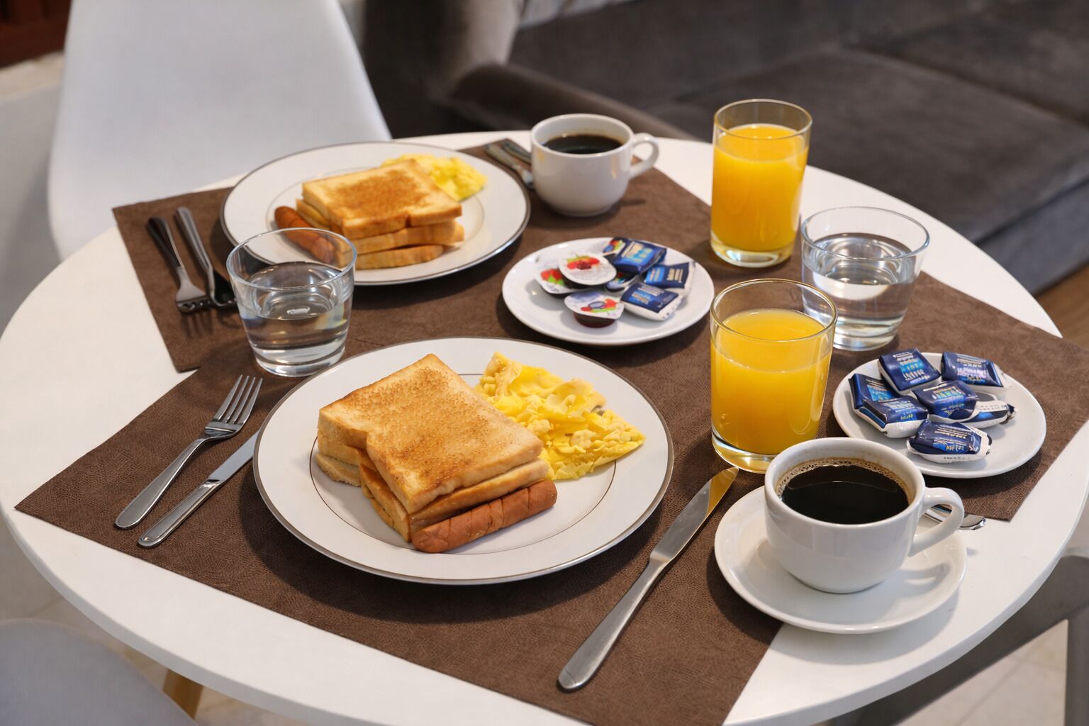A breakfast setting with toast, scrambled eggs, coffee, orange juice, and pastries on a table.