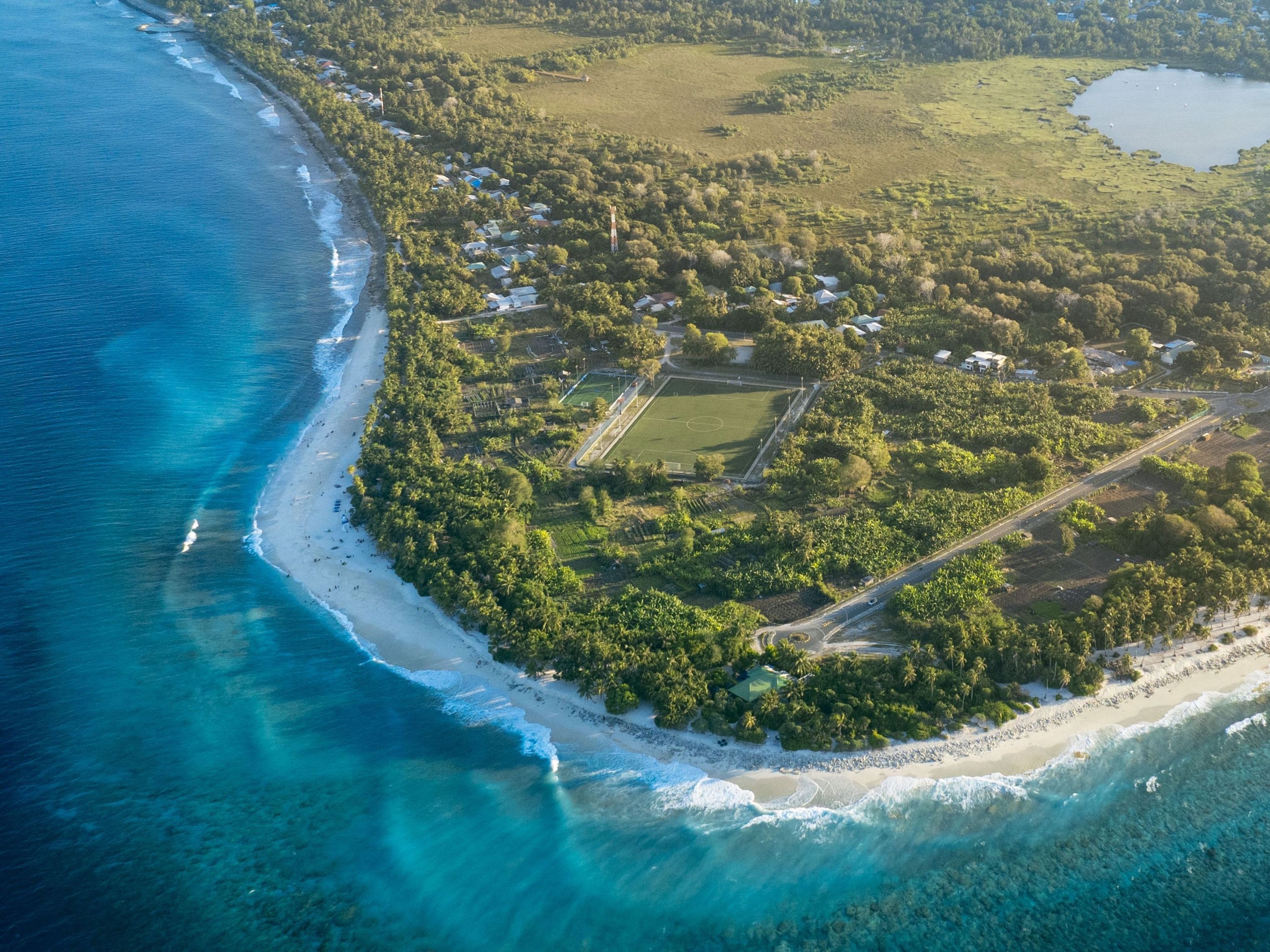 An aerial view of a coastal property with a beach, clear waters, and a mix of residential and undeveloped land.